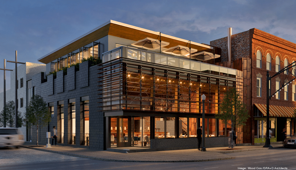 Modern two-story building with large glass windows, outdoor seating area on the rooftop, and unique architectural design, located on a city street with adjacent brick structures.