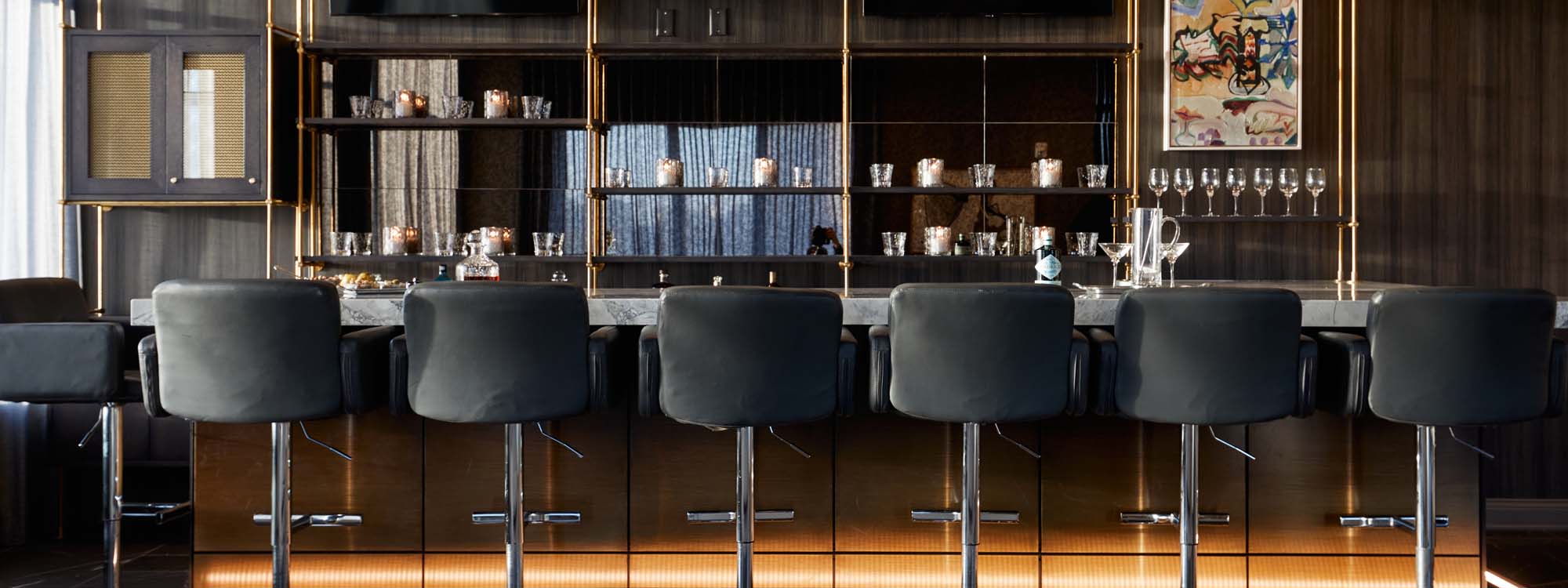 A bar with black leather stools and a wooden bar top.